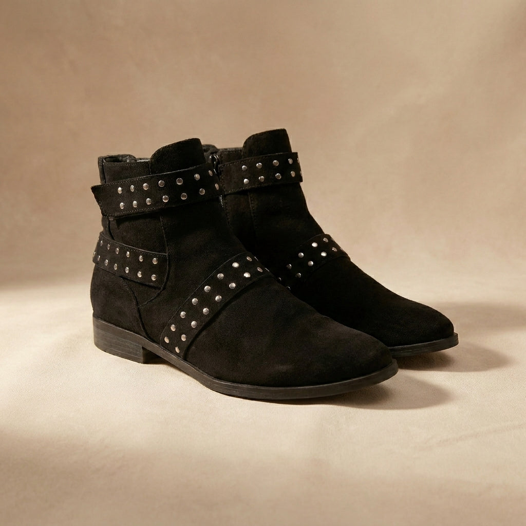 Pair of black suede ankle boots with studded details on a beige background